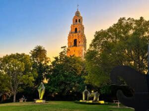 California Tower glowing in the evening sunlight above the trees and sculptures at Balboa Park in San Diego.